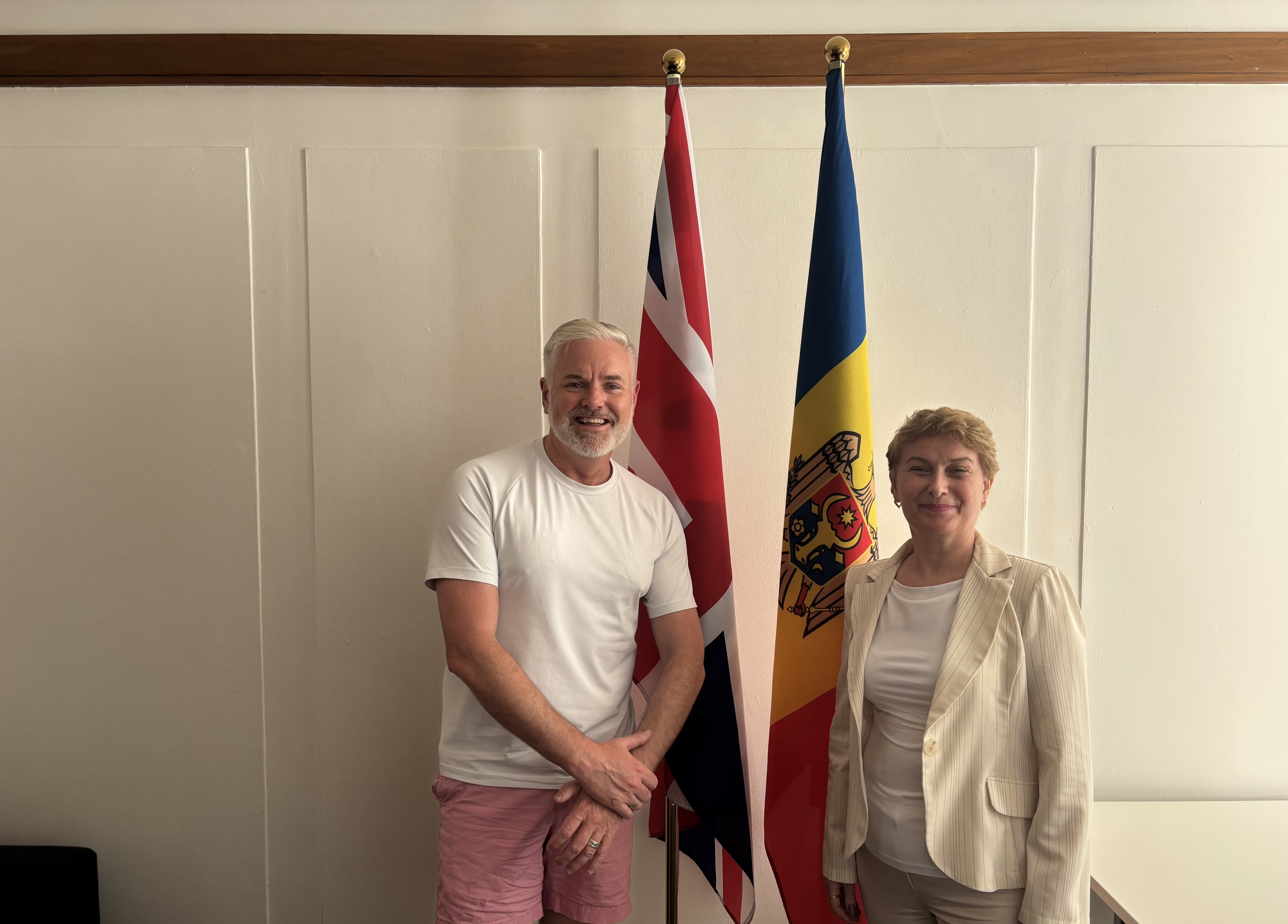 Dina Railean, Honorary Consul of the Republic of Moldova in Manchester, Salford President of Greater Manchester Chamber of Commerce and Paul Grover MBE, Export Champion for the UK Department for Business and Trade, stand together during a business meeting at the Honorary Consulate in Manchester. Positioned between the flags of the United Kingdom and the Republic of Moldova, they are pictured following discussions on strengthening UK–Moldova trade relations, supporting the Moldovan diaspora in the North West of England, promoting investment and entrepreneurship, and exploring opportunities for a future UK business delegation to Moldova Business Week. The meeting reflects ongoing collaboration to deepen commercial, economic, and cultural ties between the two countries.