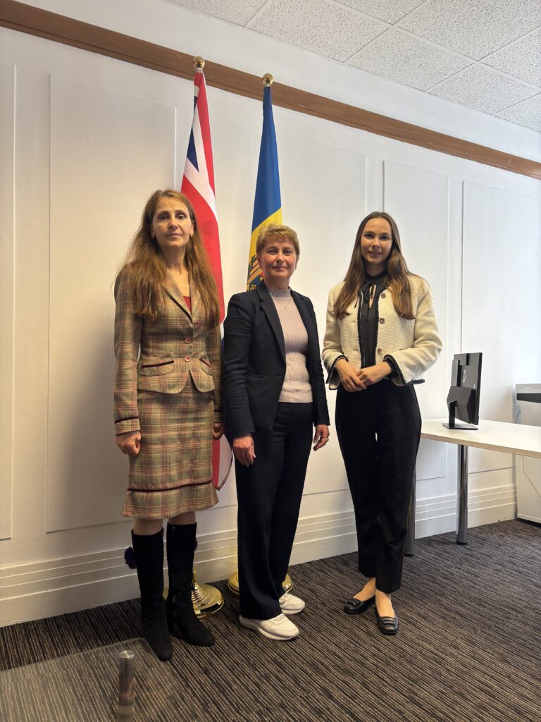 Dina Railean, Honorary Consul of the Republic of Moldova in Manchester, stands with Cristina Oleinic and a member of the Moldovan consular team at the Honorary Consulate of the Republic of Moldova in Manchester. The group is photographed in front of the flags of the United Kingdom and the Republic of Moldova during the first travelling consular outreach service hosted at the newly inaugurated Honorary Consulate on 12 June 2026. The event formed part of the Embassy of the Republic of Moldova in London's "The Embassy Comes Closer to Citizens" programme, bringing essential consular services closer to members of the Moldovan diaspora living across the North of England.