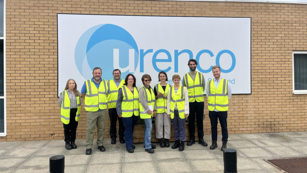 Group photograph of nine visitors, including Dina Railean, Honorary Consul of Moldova in Manchester, UK, wearing high-visibility vests outside Urenco UK’s Capenhurst facility in Cheshire on 24 July 2026. The delegation stands in front of a large Urenco sign following a Liverpool Consular Corps visit focused on nuclear fuel production, energy security, safety, precision and international cooperation.