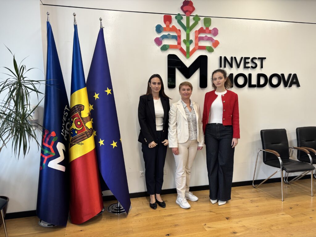 Dina Railean, Honorary Consul of Moldova in Manchester, with Invest Moldova economic diplomacy representatives Ana-Maria Cenuș and Gabriela Romanciuc at the agency’s Chisinau office. They stand beside the Invest Moldova, Moldovan and European Union flags beneath the Tree of Life and Invest Moldova branding.