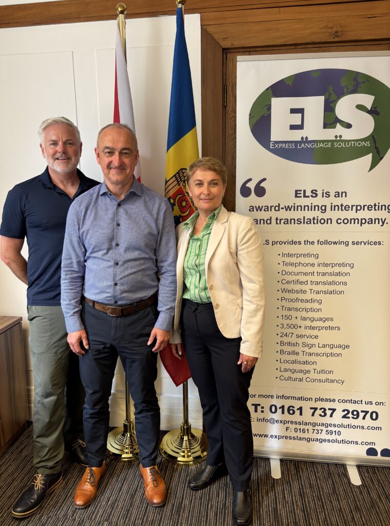 Paul Kallee-Grover MBE, Murray Mathieson of Positively Legal and Dina Railean, Honorary Consul of the Republic of Moldova in Manchester, meet at the Honorary Consulate on 28 August 2026 to prepare for the First UK Business-Led Trade Mission to Moldova. They stand beside the UK and Moldovan flags and an Express Language Solutions display.