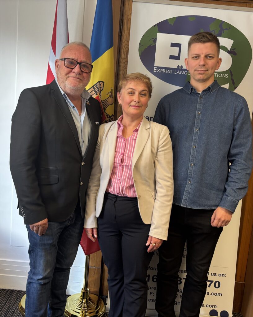 Derrek Johnston, Director of Data Safe Solutions Ltd, Dina Railean, Honorary Consul of the Republic of Moldova in Manchester, and Krzysztof Golowacz, Product Manager at Data Safe Solutions Ltd, meet at the Honorary Consulate on 19 October 2026 to discuss post-mission support and the company’s plans to explore the Moldovan market. The British and Moldovan flags and Express Language Solutions branding appear behind them.